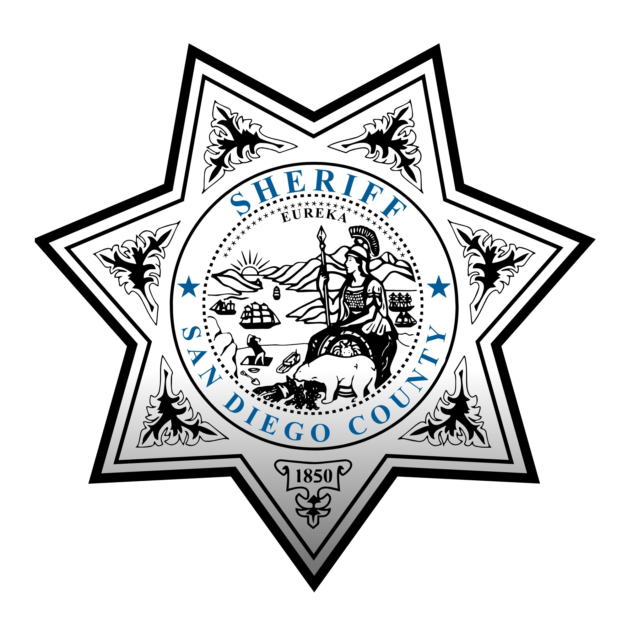 A group of nine people stand together in front of a wall with text that reads “San Diego County Sheriff.” The group includes individuals in uniforms and professional clothing, standing side by side and facing the camera. The background is a simple indoor setting with neutral walls and flooring.