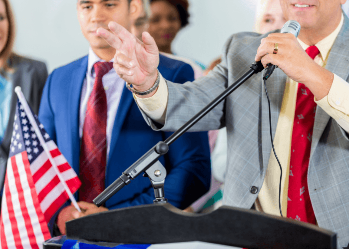 A photo of a man in a suit talking into a microphone at a podium.