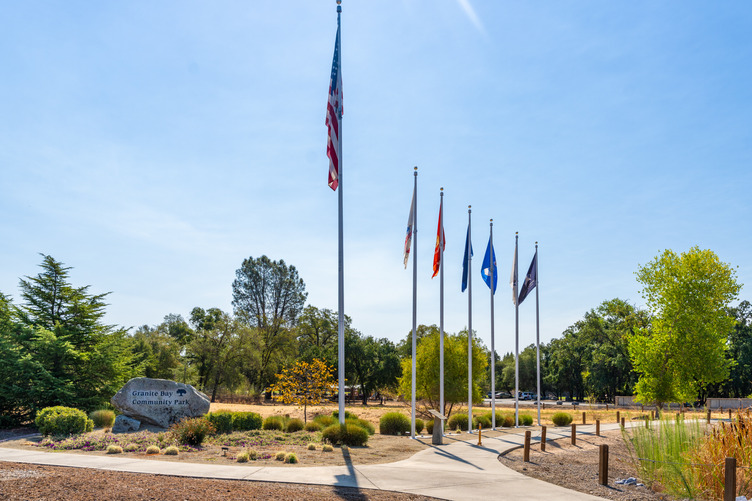 A photo of a variety of flags including the American flag, military service flags, a POW/MIA flag, and memorial benches at the Granite Bay Community Park.