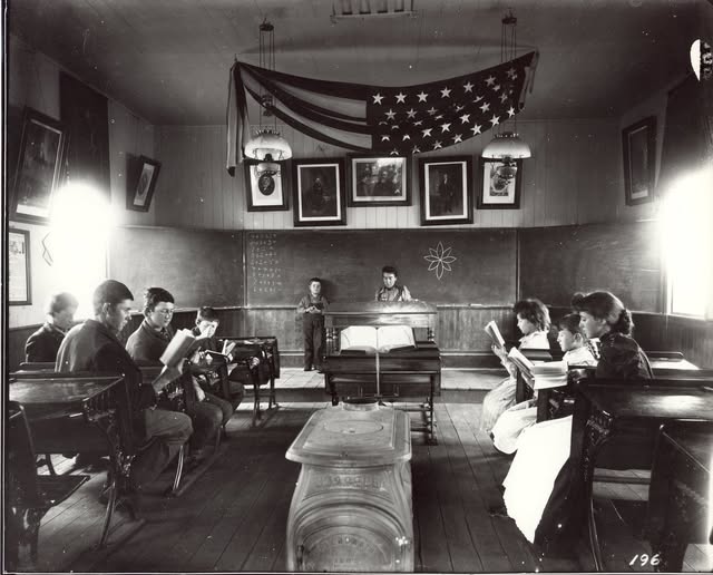 A black and photo of a historic schoolroom with students in it.