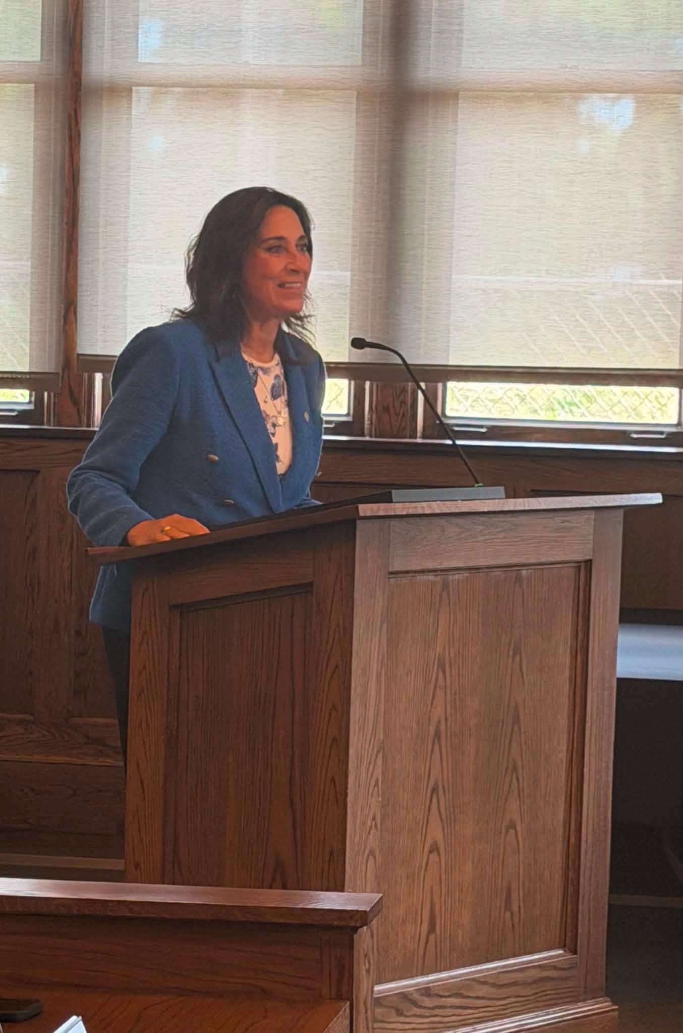 State Representative Angela Witwer standing and smiling behind a podium as she speaks to a crowd.