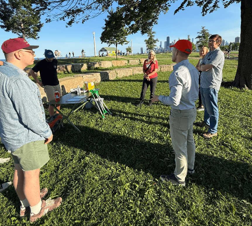 Alderman Timmy Knudsen speaks with a group of community members in a lakefront park, with the Chicago skyline visible in the background.