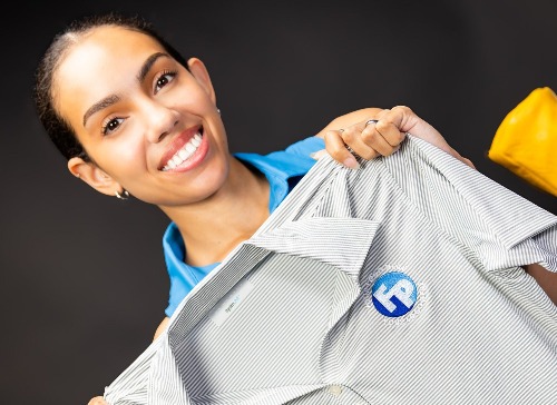 A woman holding up a grey striped shirt with a blue embroirdered on Fully Promoted logo.