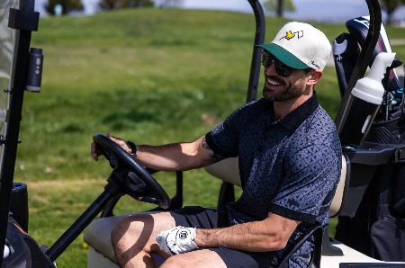 A man on a golf cart wearing and embroidered branded hat.