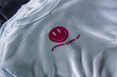 A white t-shirt with a pink smiley face loGo and a Spotlight Dance Cup phrase placed on it DTF