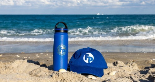 A fully promoted branded blue hat and water bottle placed on the sand in the beach.