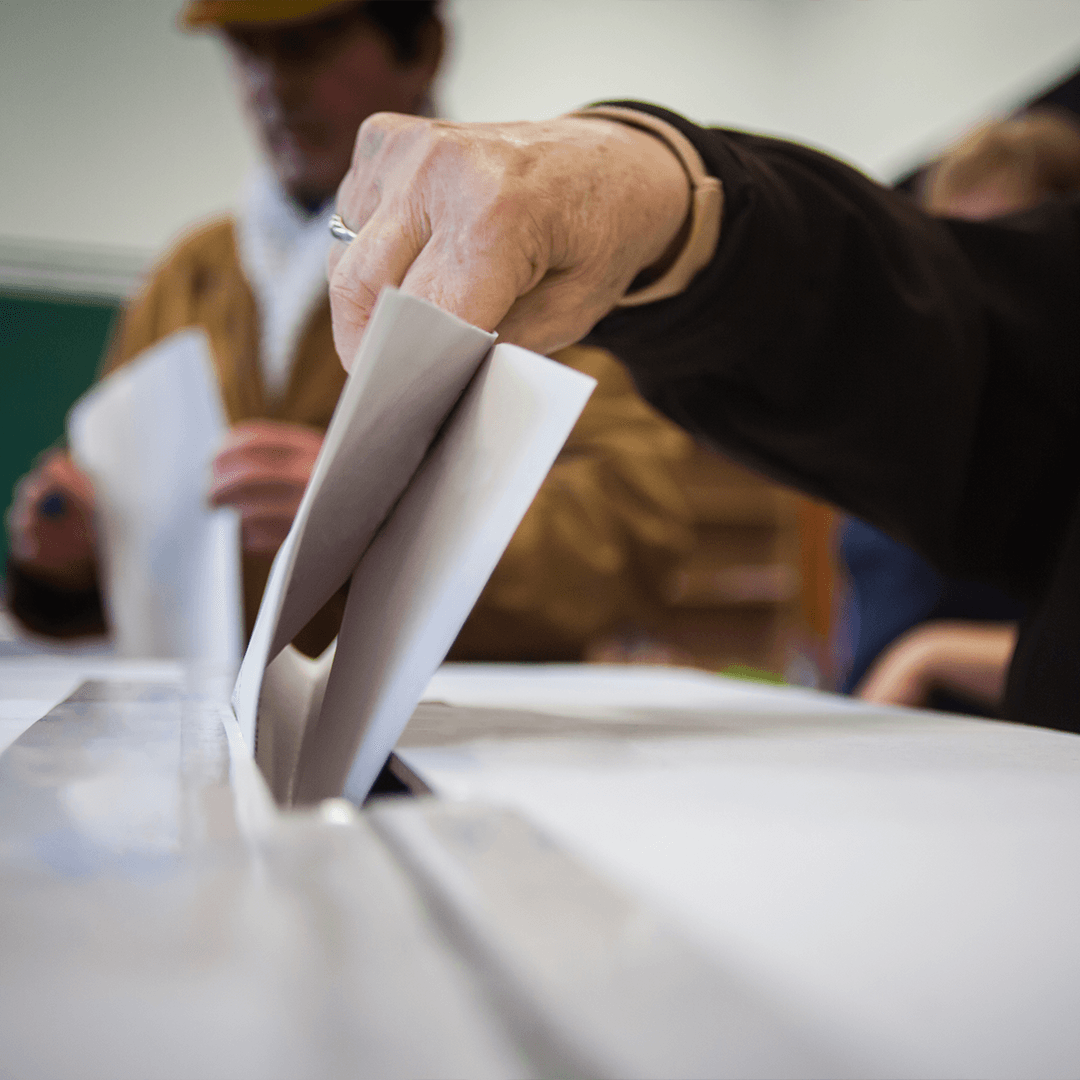 A hand depositing an official ballot into a ballot box slot. A hand depositing an official ballot into a ballot box slot.