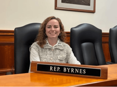 Rep. Byrnes sits at a table with a placard with her name on it. Rep. Byrnes sits at a table with a placard with her name on it.