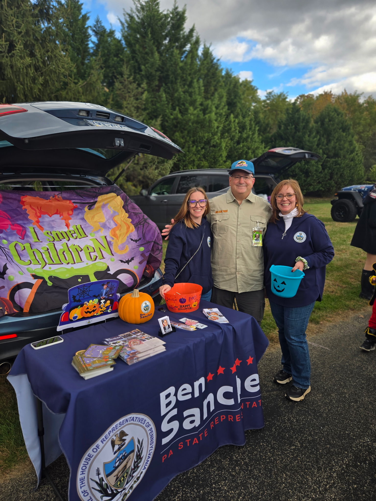 Rep. Sanchez standing at his trunk set up with two staff members.