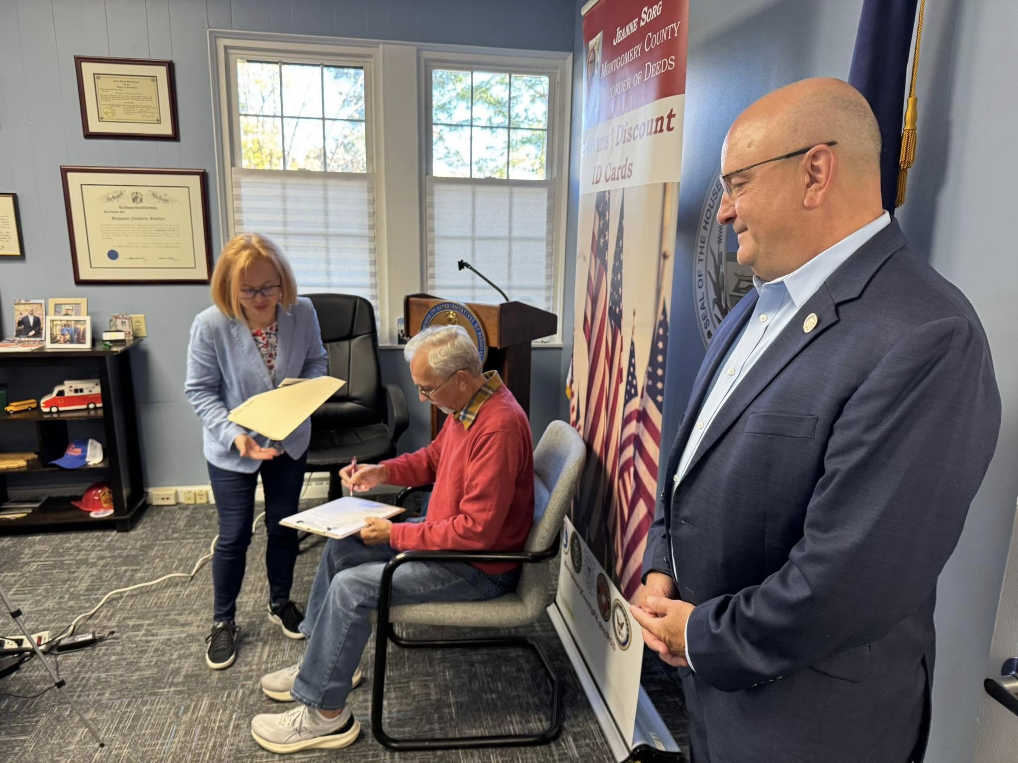 a photo of Recorder of Deeds Jean Sorg helping a constituent register for the Veteran Discount ID while Rep. Sanchez looks on.