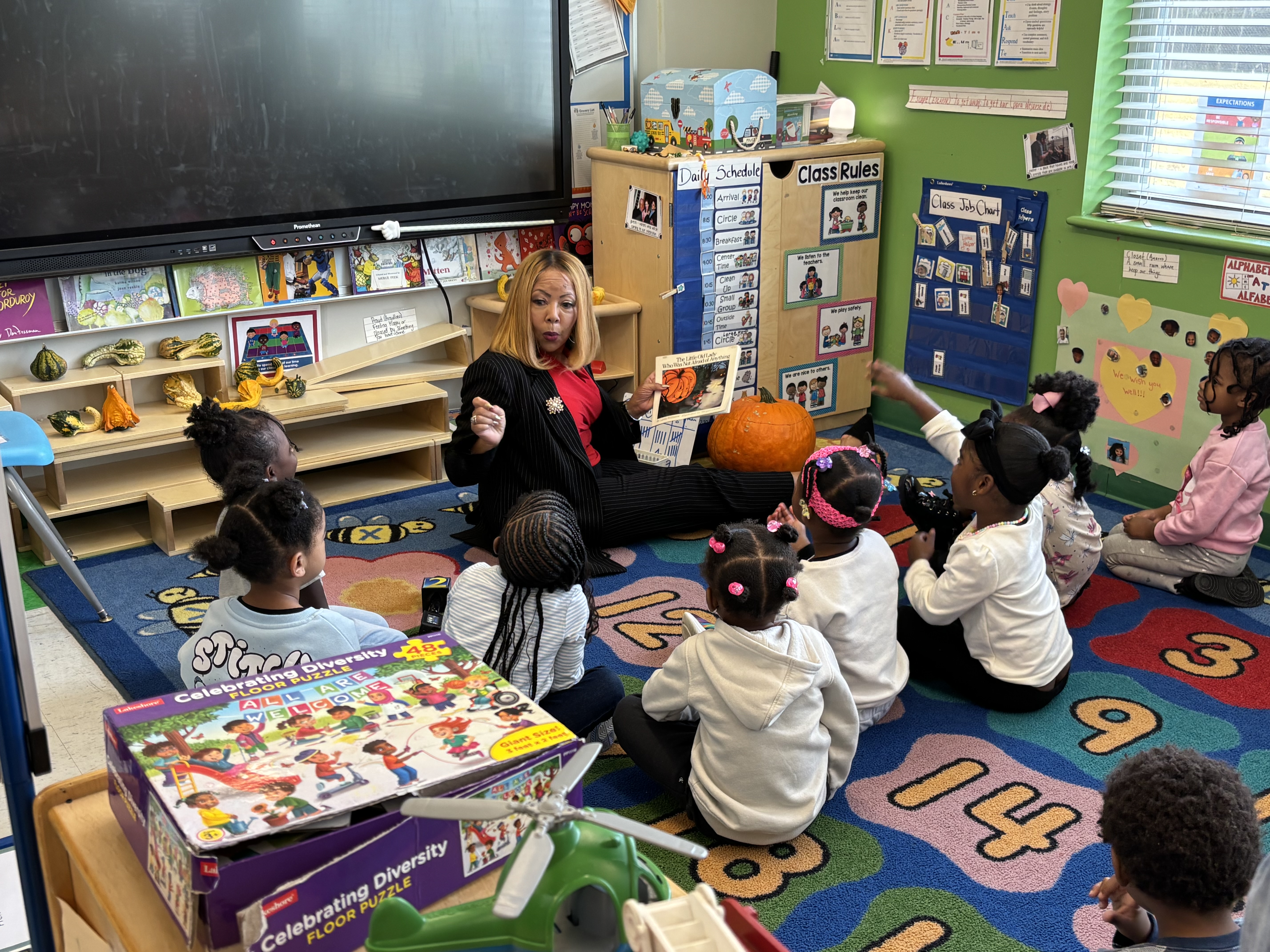 Congresswoman McBath sits on the floor with children as she reads a book to them.