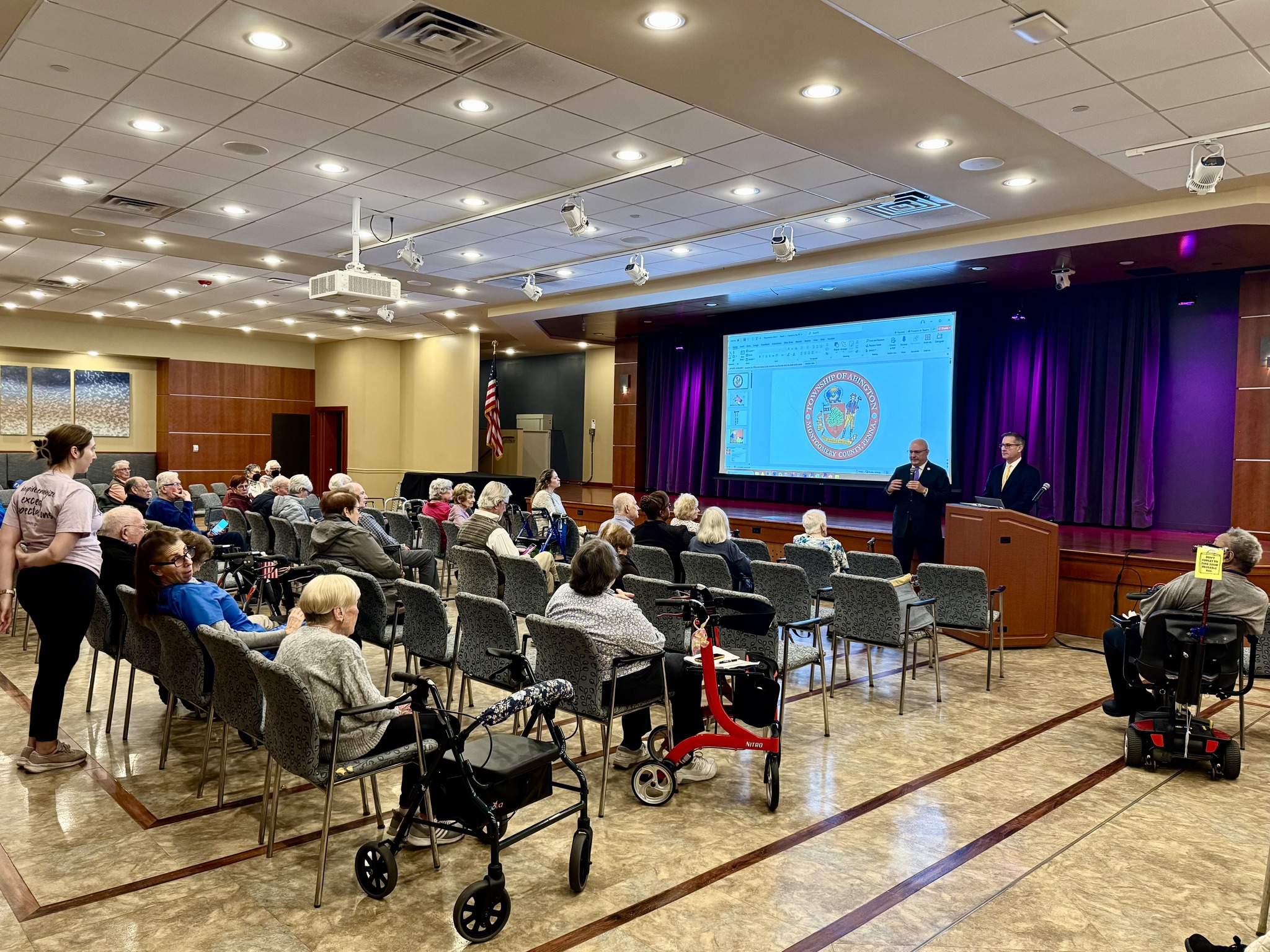 An image of a crowded room from the back with Rep Sancehz and Commissioner Winegrad at the front speaking to everyone.