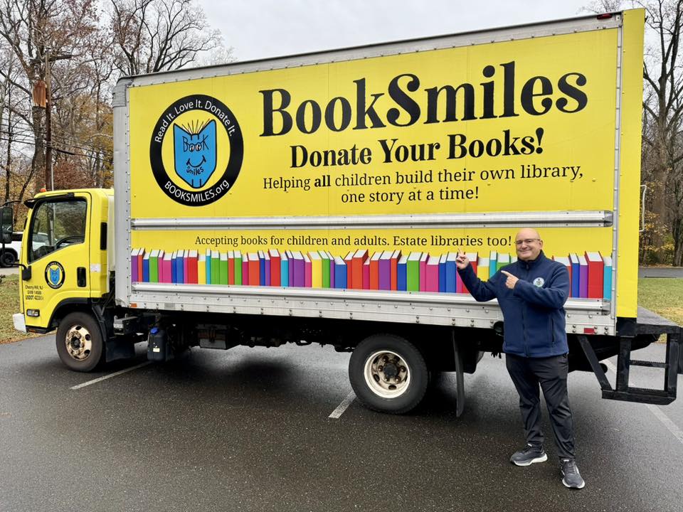 Image of Rep. Sanchez standing and pointing up to the Book Smiles Truck behind him.