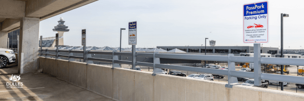 View from a parking garage at Dulles International Airport, featuring signs for "Park Premium Parking Only," with parked cars visible and the airport's iconic observation tower in the distance.