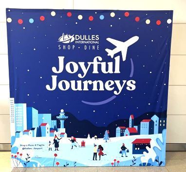 Promotional display at Dulles International Airport featuring the text 'Joyful Journeys' with a colorful illustration of a winter holiday scene at an airport, including travelers and an air traffic control tower.
