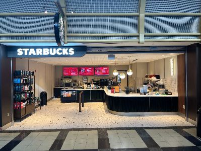 Interior view of a Starbucks, featuring a fully stocked counter, a menu display, and a variety of merchandise on display.