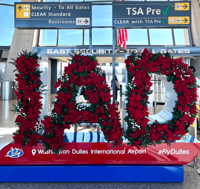 Holiday wreath decorations spelling out "IAD" at Washington Dulles International Airport, set under a sign indicating TSA Pre and CLEAR locations by East Security Gate Entrance