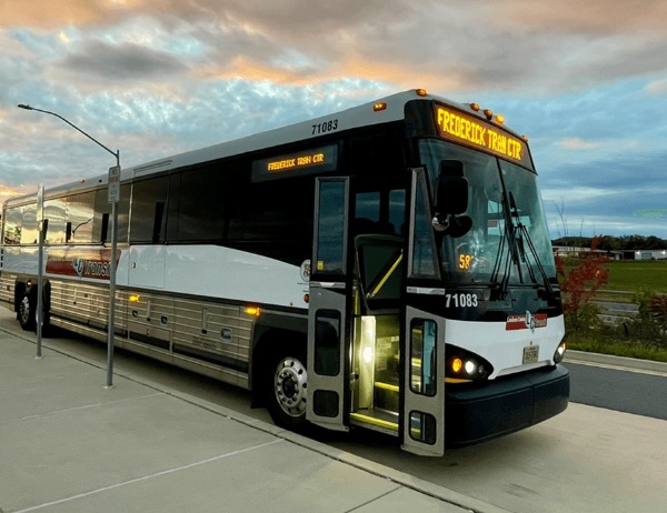 A commuter bus at a transit stop from Dale City. The doors are open, and the bus is parked under a cloudy sky at dusk.