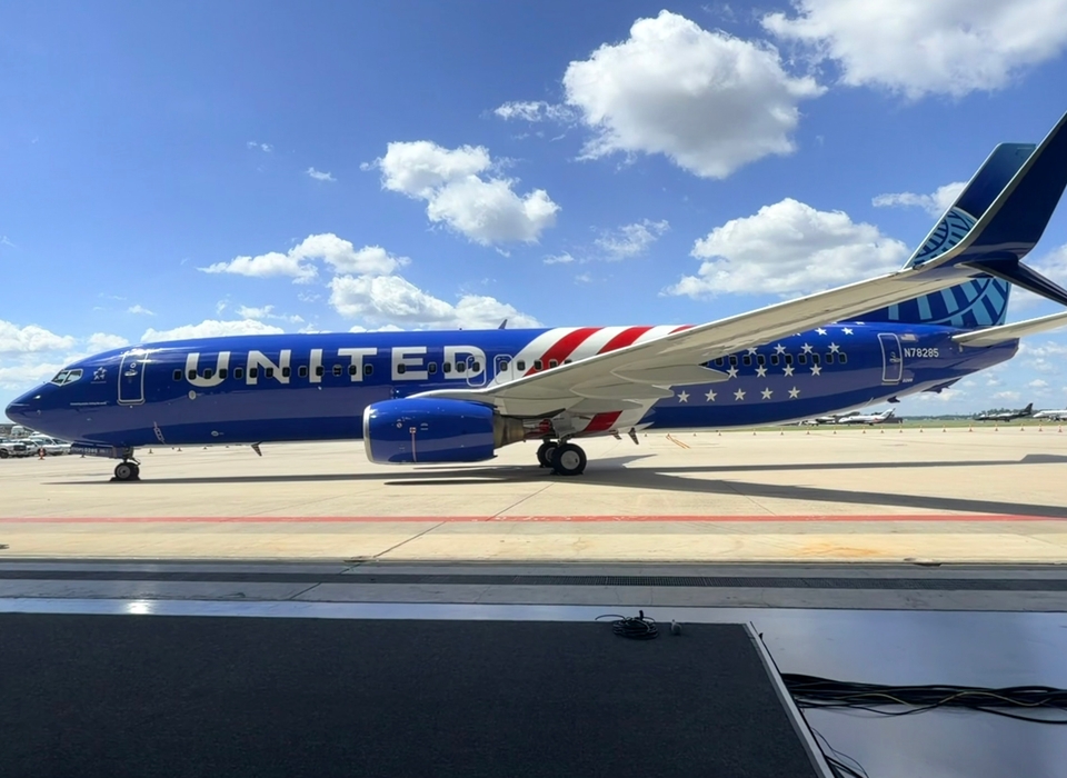 A United Airlines plane with a distinctive blue and red design, featuring stars and stripes, is parked on Dulles International airport tarmac under a clear sky with scattered clouds.