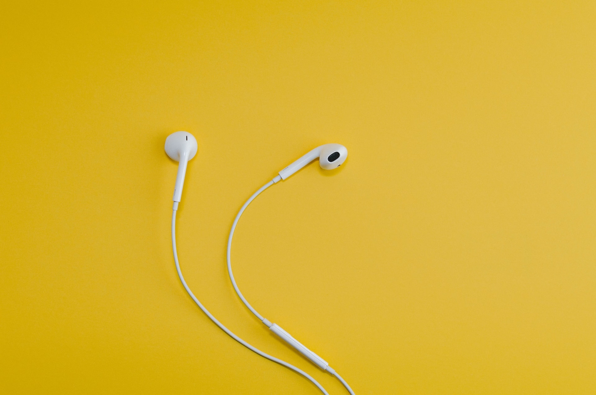 Sarı bir yüzeyin üstünde klasik bir Apple kablolu kulaklık duruyor.
