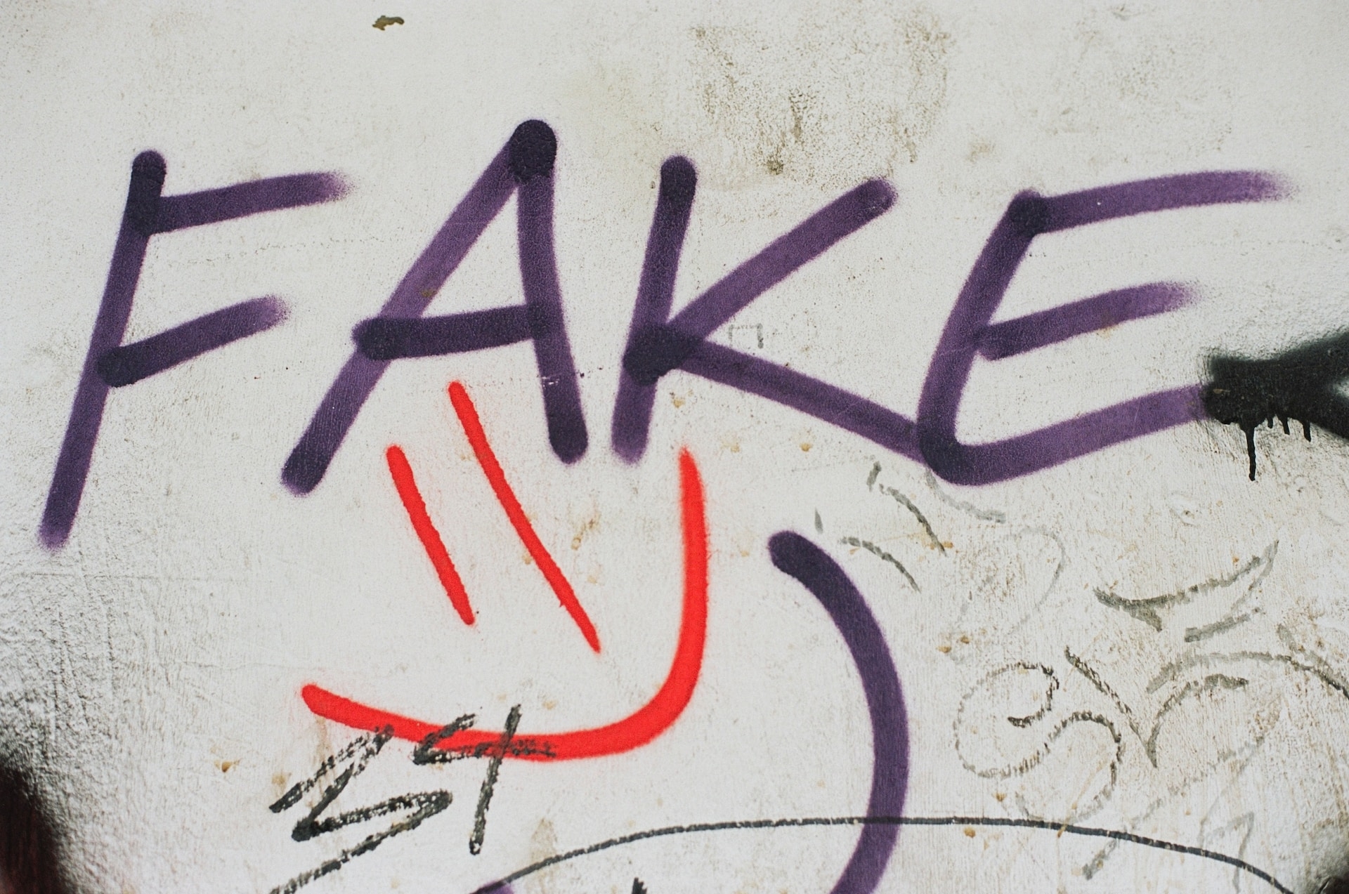 Bir duvardaki graffitide mor renkte fake yazılmış. Altında da kırmızı renkle gülen bir yüz çizilmiş.