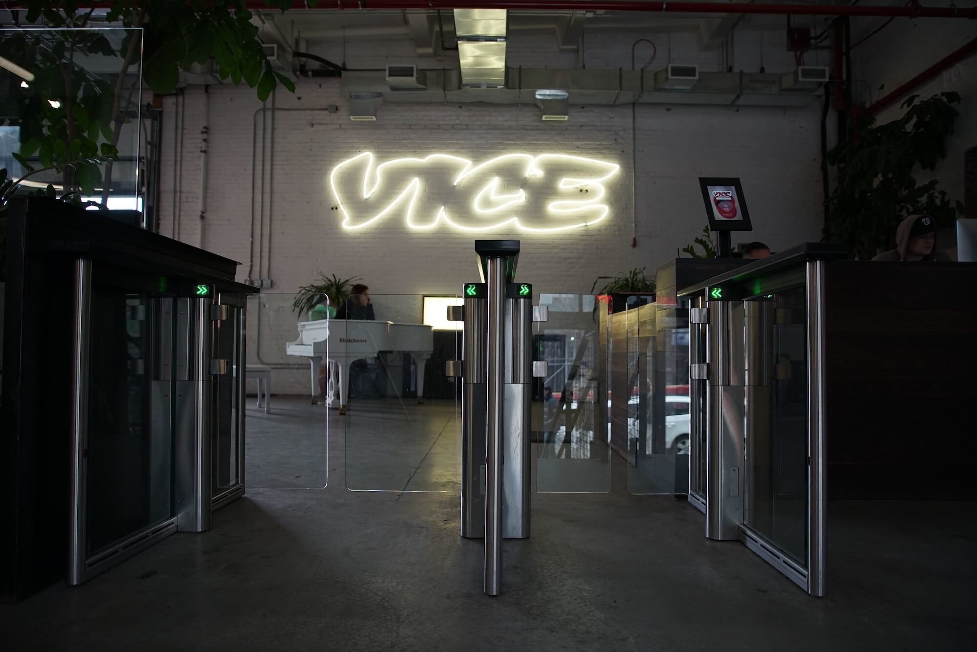Vice ofislerinin girişinden çekilmiş bir fotoğraf. Güvenlik kapılarının arkasındaki beyaz duvarda LED ışıklarla yazılmış Vice logosu görülüyor.