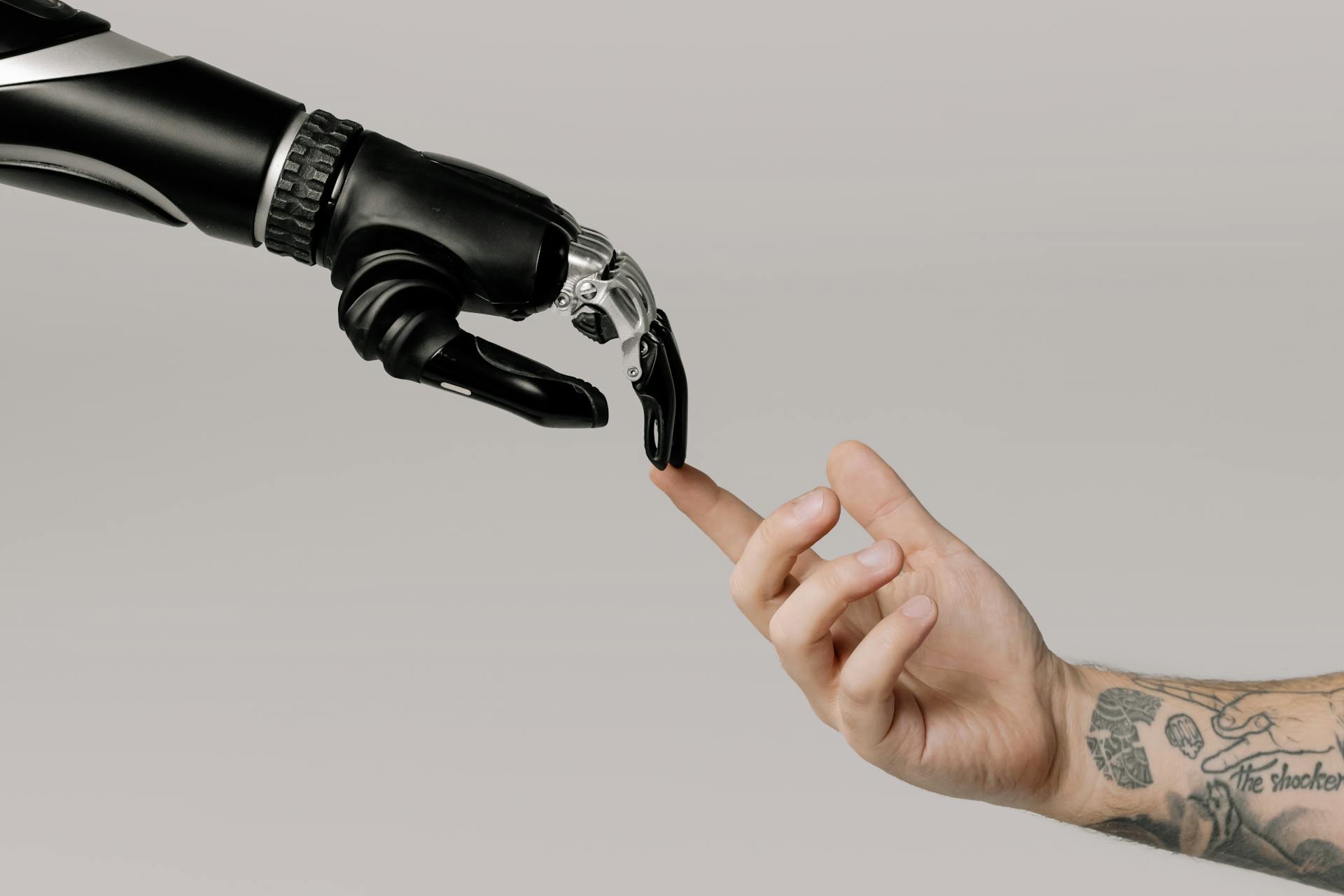 Beyaz arka planın önünde üstten uzanan robot bir el ile alttan uzanan bir insan elinin parmakları birbirine dokunuyor.