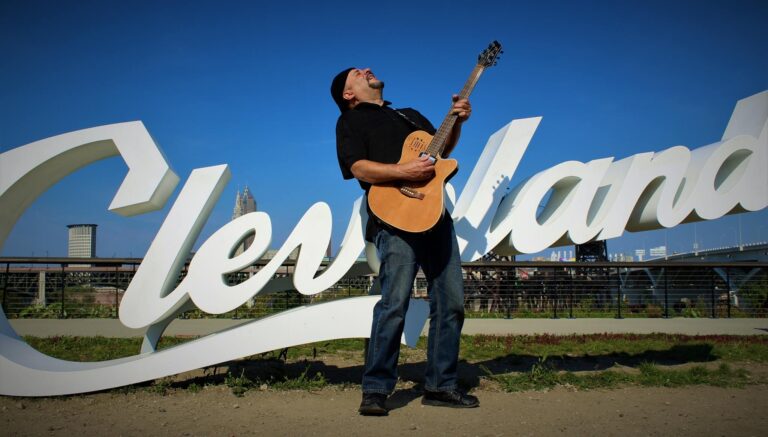 Man playing guitar in front of "Cleveland" sign.